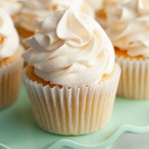 A yellow cupcake with white frosting on a teal cake stand.
