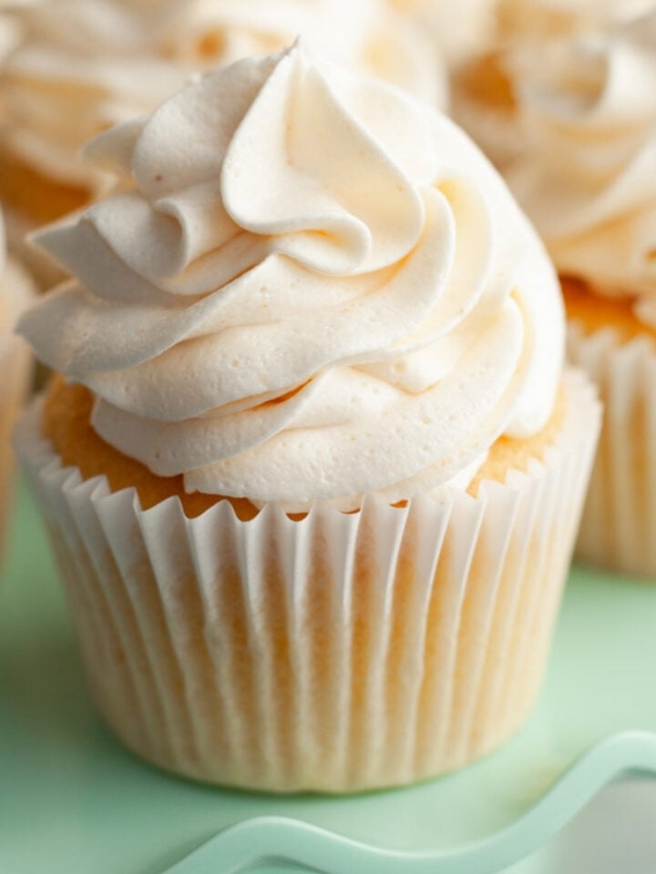 A yellow cupcake with white frosting on a teal cake stand.