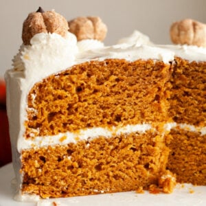A pumpkin cake with cream cheese frosting with a mini pumpkin decoration on top.