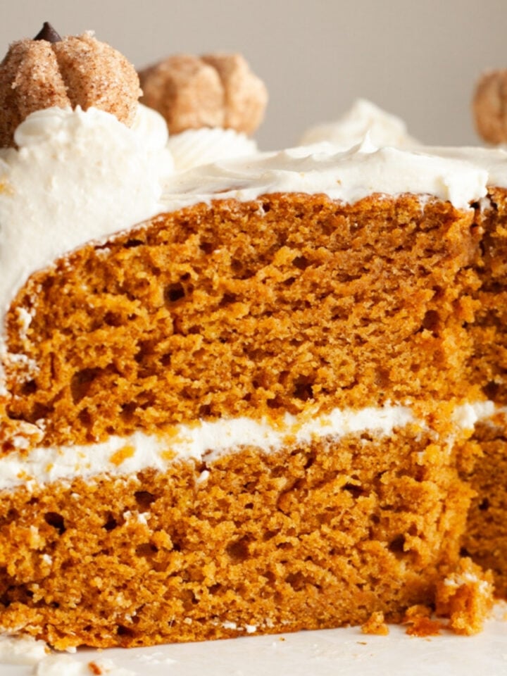 A pumpkin cake with cream cheese frosting with a mini pumpkin decoration on top.