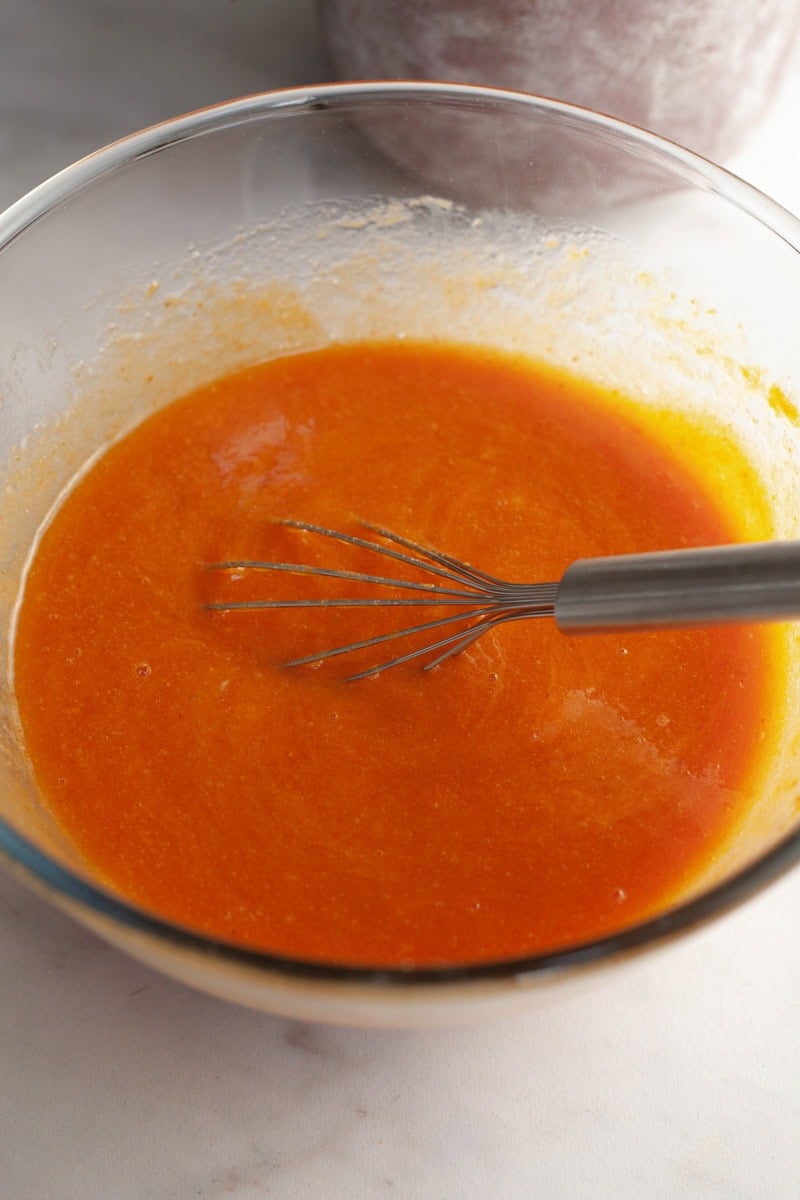 Pumpkin cake batter in a glass bowl with a whisk.