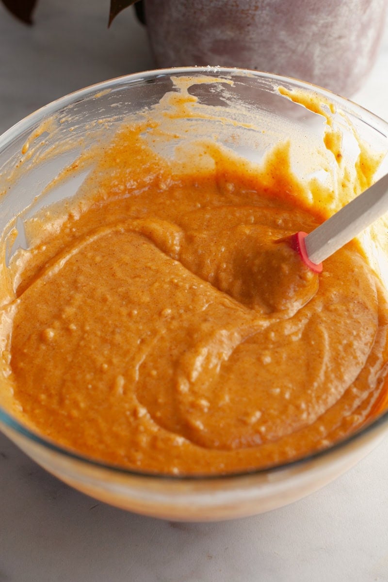 Pumpkin cake batter in a glass bowl with a rubber spatula.