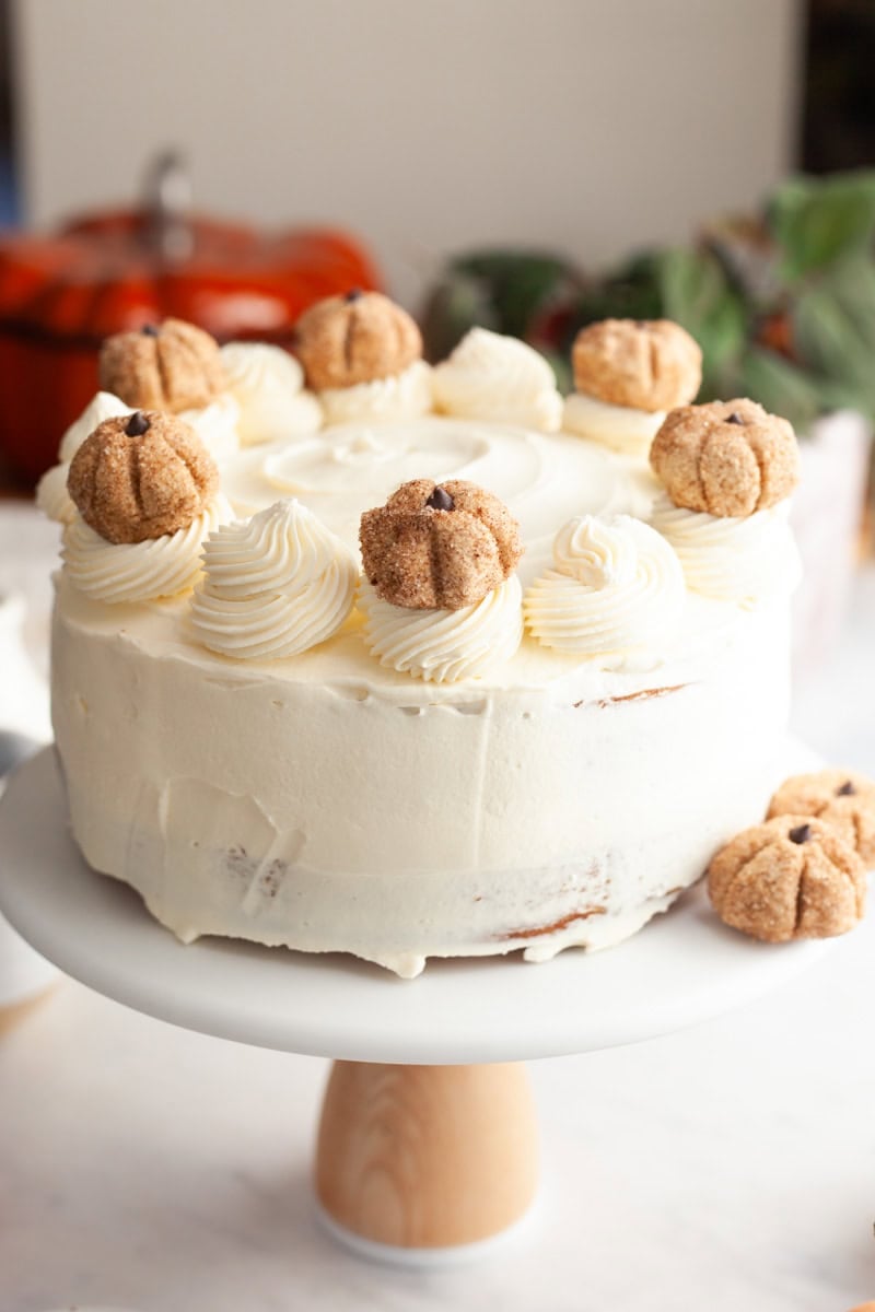 A cake covered in cream cheese frosting, deocrated with pumpkin cookie dough pumpkins.