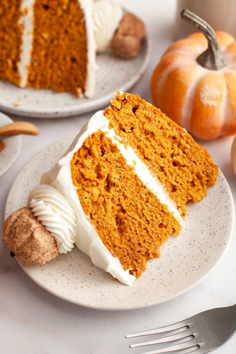 A slice of pumpkin cake with cream cheese frosting on a small plate.